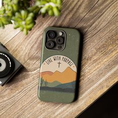 a phone case sitting on top of a wooden table next to a camera and plant