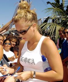 a woman in white tank top writing on her cell phone while people watch from the side