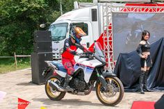 a person on a motorcycle in front of a truck with a woman standing next to it