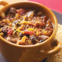 a yellow bowl filled with chili and cheese sitting on top of a piece of bread