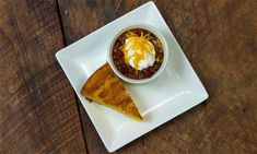 a white plate topped with a slice of pizza and a bowl of chili cheese soup