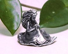 a silver figurine sitting on top of a table next to a green leaf