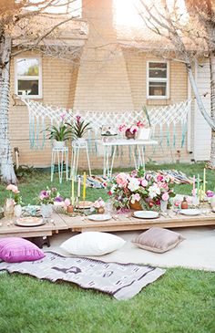 an outdoor picnic setting with flowers and candles on the table, in front of a house