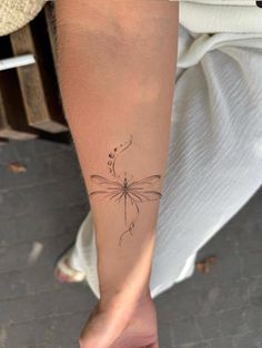 a woman's arm with a small dragonfly tattoo on it