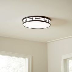 a round light fixture hanging from the ceiling in a room with white walls and windows