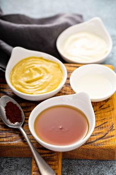 three bowls with different types of sauces on a cutting board next to spoons