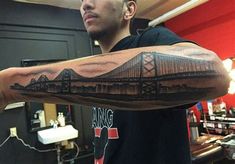 a man with a tattoo on his arm that has a bridge in the background and water below it