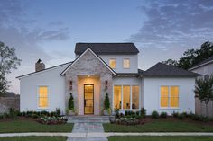 a white brick house with yellow windows and plants in front of it at night time