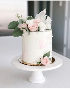 a white cake with pink flowers and greenery on top is sitting on a plate