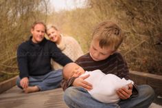 a man holding a baby while sitting on a wooden bridge with two women and a boy