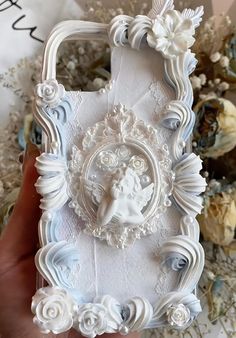 a hand holding a white phone case with an angel in the center and flowers around it