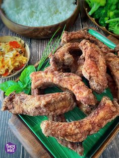 some fried food is on a green plate and next to bowls of rice, broccoli and other vegetables