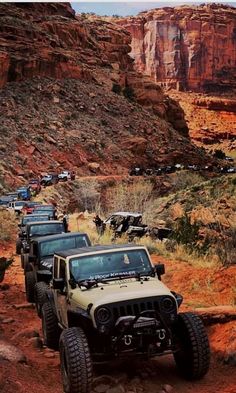 four jeeps driving down a dirt road in the desert with mountains and cliffs behind them