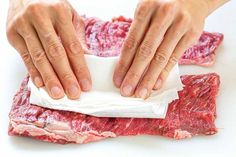 two hands on top of raw meat and one hand holding a piece of white paper