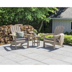 two chairs and a table on a patio with firewood stacked in the back ground