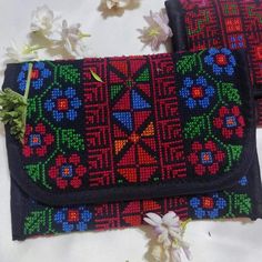 two embroidered bags sitting on top of a white cloth covered table with flowers and leaves