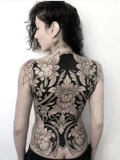 a woman with tattoos on her back is standing in front of a white wall and looking at the camera