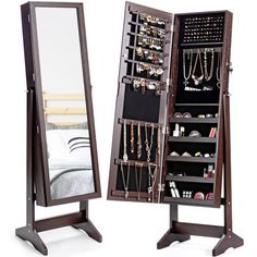 a wooden jewelry cabinet sitting next to a mirror on top of a stand with necklaces and bracelets hanging from it