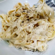 a white plate topped with pasta covered in sauce and seasoning next to a fork