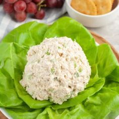 a white plate topped with lettuce covered in cheese next to grapes and crackers