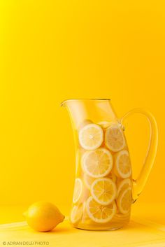 a pitcher filled with lemons sitting on top of a yellow table next to two lemons