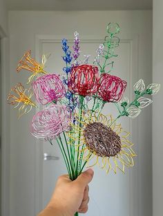 a hand holding a vase filled with lots of different colored wire art work on top of a table