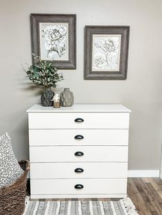 a white dresser sitting next to two framed pictures