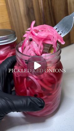 a person in black gloves holding a jar filled with pickled onions next to a knife