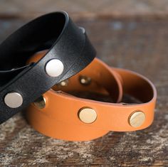 two leather bracelets with gold dots on them sitting on top of a wooden table