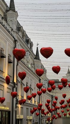 many red hearts are hanging from the side of buildings in an urban area with lights strung above them