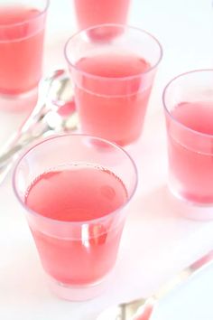 four glasses filled with pink liquid on top of a white tablecloth next to spoons