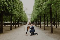 a man and woman are kissing in the middle of a tree lined road with trees lining both sides