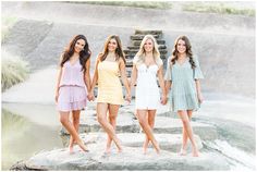 three beautiful young women standing next to each other on top of a rock formation in front of a body of water