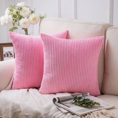 two pink pillows sitting on top of a white couch next to a vase with flowers