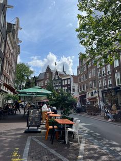 people are sitting at an outdoor table in the middle of a city street with buildings on both sides