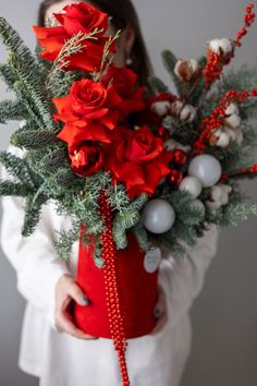 a woman holding a bouquet of red roses and greenery in her hands while wearing a white shirt