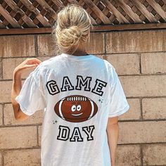 a woman standing in front of a brick wall wearing a game day t - shirt