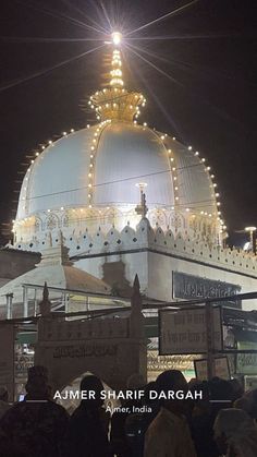 people are standing in front of a large white building with lights on it's roof