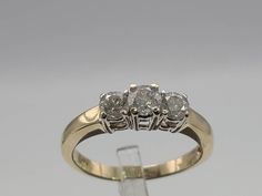 a three stone diamond ring on a clear display stand, with the top setting in yellow gold