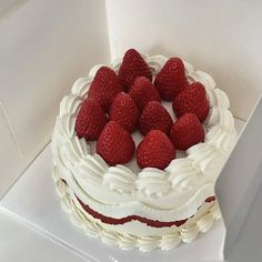 there is a cake with white frosting and strawberries on the top, sitting in a box