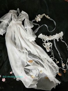 a white dress and necklaces are laying on a black cloth with flowers in the background