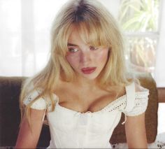 a woman with blonde hair wearing a white dress and posing for a photo in front of a window