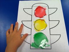 a child's hand is holding up a piece of paper with a traffic light drawn on it