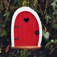 a red door with a heart on it in the middle of some grass and trees