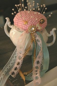 a tea pot with some pins in it on top of a table next to a ribbon