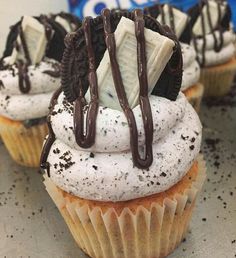 cupcakes with white frosting and chocolate drizzled on top are sitting on a table