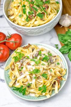 two plates of pasta with mushrooms, tomatoes and parsley on a marble countertop