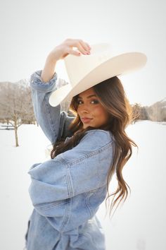 a woman wearing a white cowboy hat and denim jacket posing for a photo in the snow