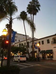 cars are parked on the street in front of palm trees and buildings at sunset or dawn