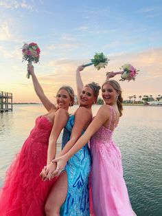 three beautiful young women standing next to each other on a dock holding bouquets in their hands